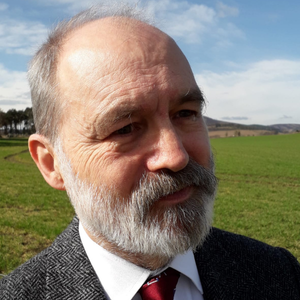 A portrait of author Graham Cooper standing in a lush green field. 