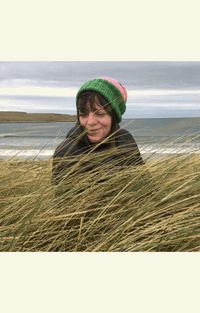 Rebecca Marr in a green hat, smiling among tall grass by the sea.