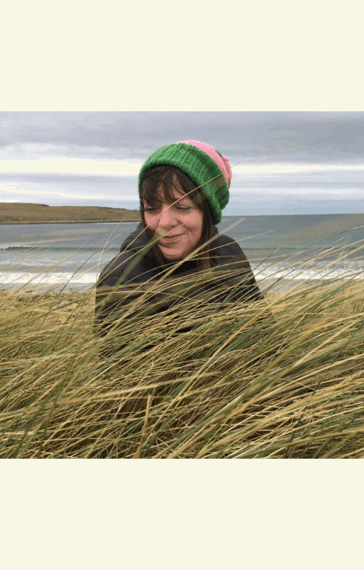 Rebecca Marr in a green hat, smiling among tall grass by the sea.